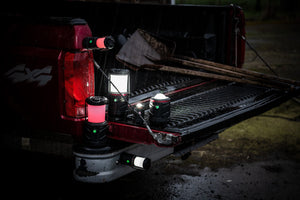 A collection of LED emergency area lanterns sitting on and magnetically mounted on the bed of a truck in the rain, the area lights have white and red lights. 