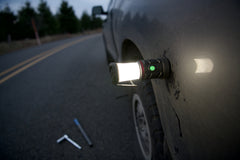 An illuminated LED lantern attached by magnets to a car above a flat tire, lifestyle photo.