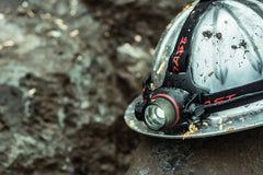 LED Headlamp Mounted on Wet and Dirty Hard Hat Sitting on a Wet Rock, lifestyle photo