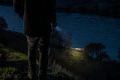 Man Shining LED Flashlight at Empty Boat on River Bank, lifestyle photo